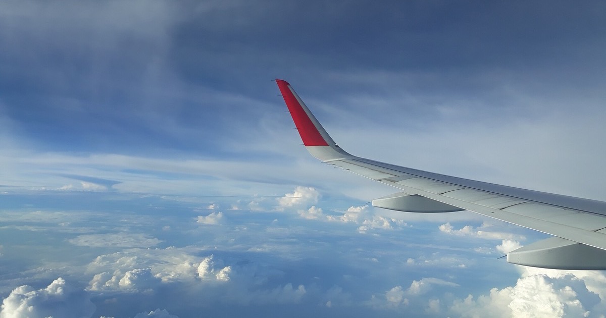 An airplane wing with a red winglet above a bank of clouds