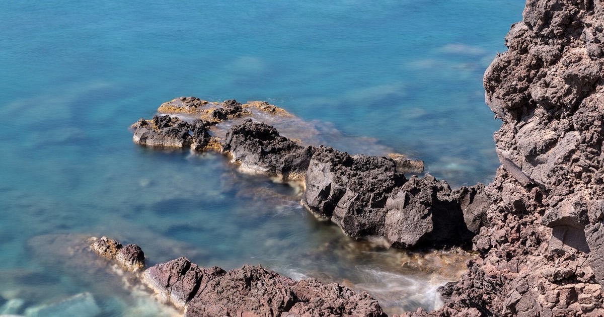 Volcanic rocks meeting clear turquoise water on a quiet Mediterranean coast